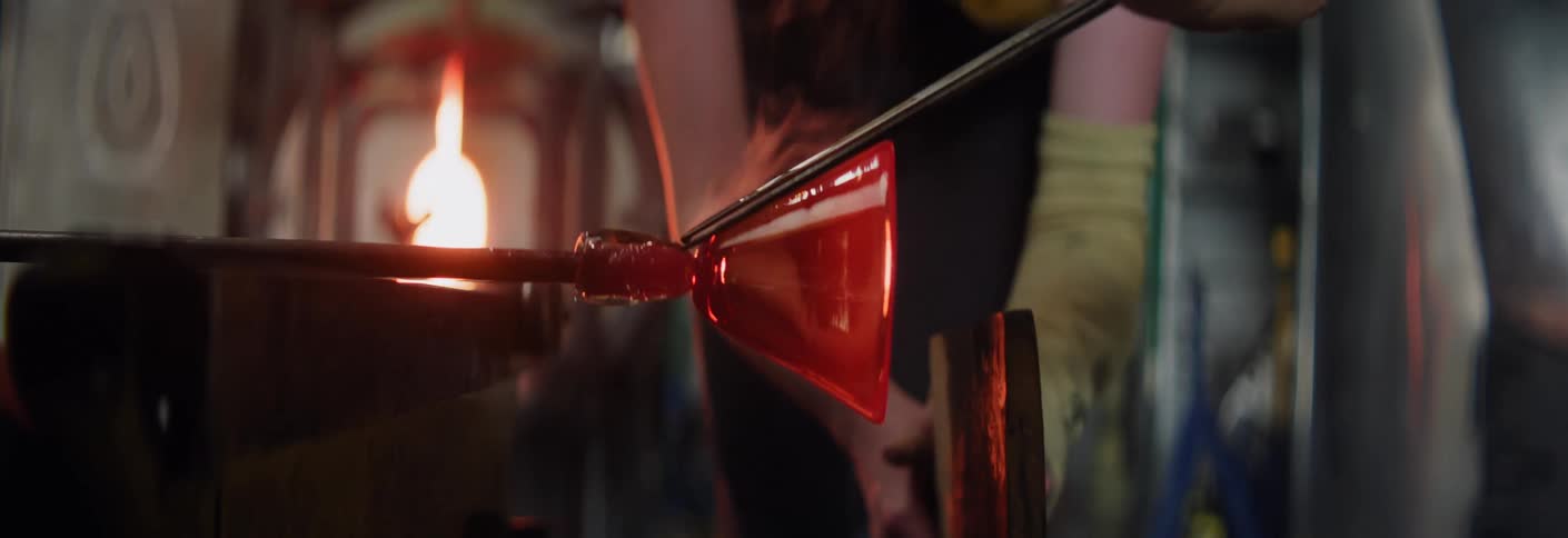 Molten glass being shaped with tongs and a rod in a glassblowing workshop