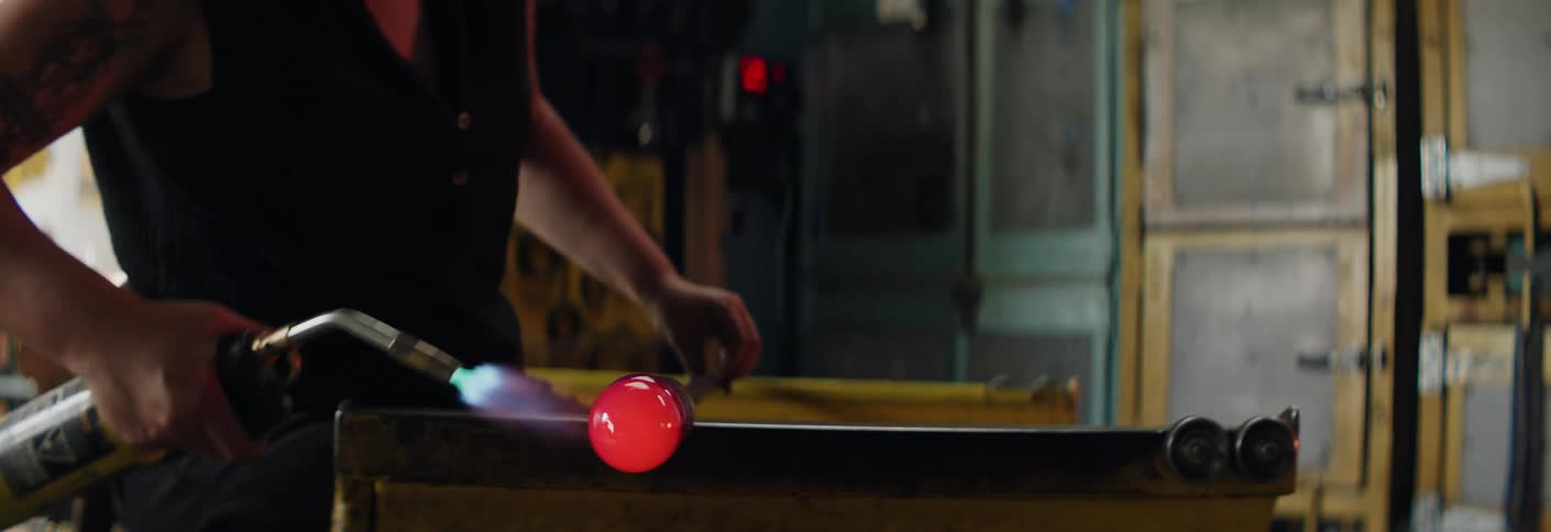 A woman uses glass shaping tools on a glowing metal rod
