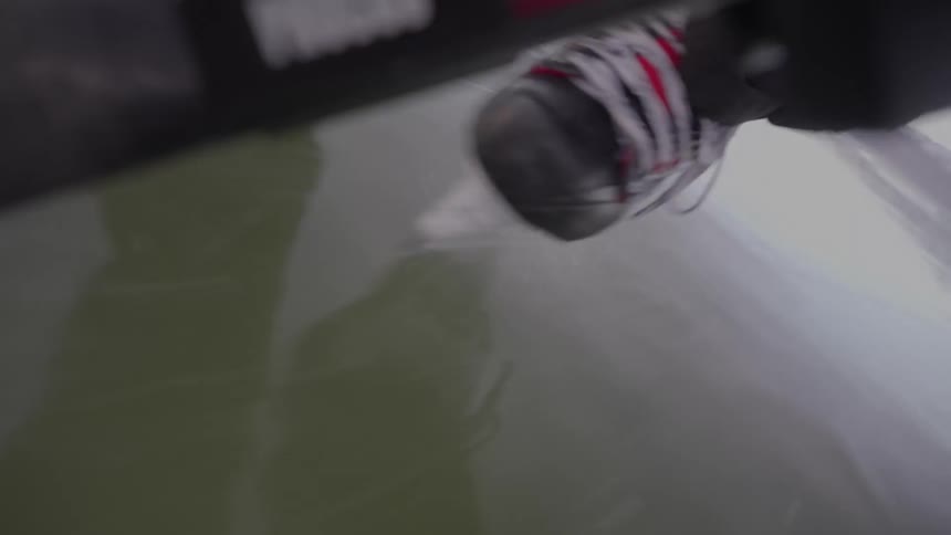 A closeup captures a hockey skate carving into the ice as a stick and reflections blur across the frozen surface