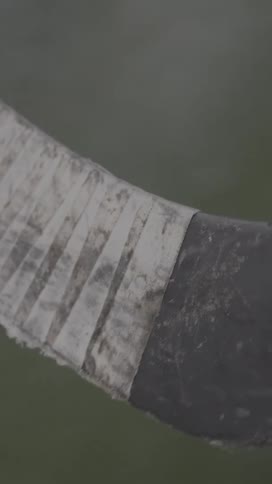 A closeup shows a taped hockey skate blade dusted with ice with a puck resting to the left on the frozen surface