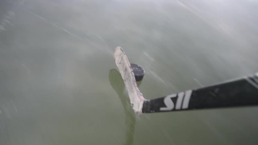 A hockey stick strikes a puck on the ice in a closeup action shot