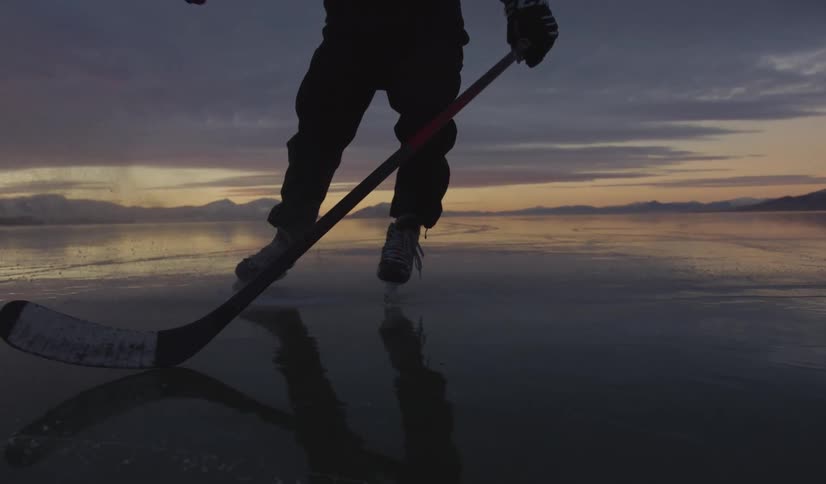 Person with skates and hockey stick on frozen surface at dusk