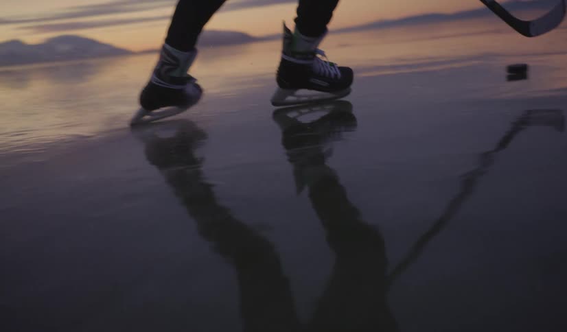Person with skates and hockey stick on frozen lake at sunset