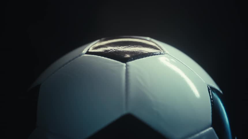 A whiteandblack soccer ball rests on a platform illuminated by a strong light that reflects cleanly across its surface