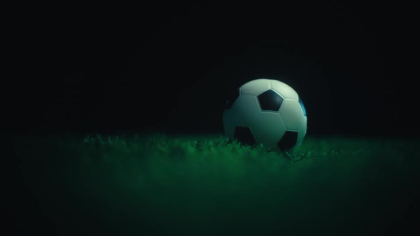 Soccer ball on grass lit from the side in dark setting