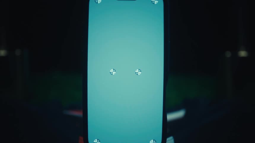 A close up shot of a smartphone with a bright light blue screen featuring several small tracking markers positioned against a dark background