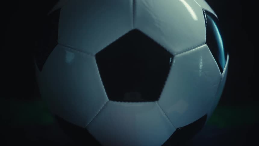 A whiteandblack soccer ball rests on a platform illuminated by a strong light that reflects cleanly across its surface