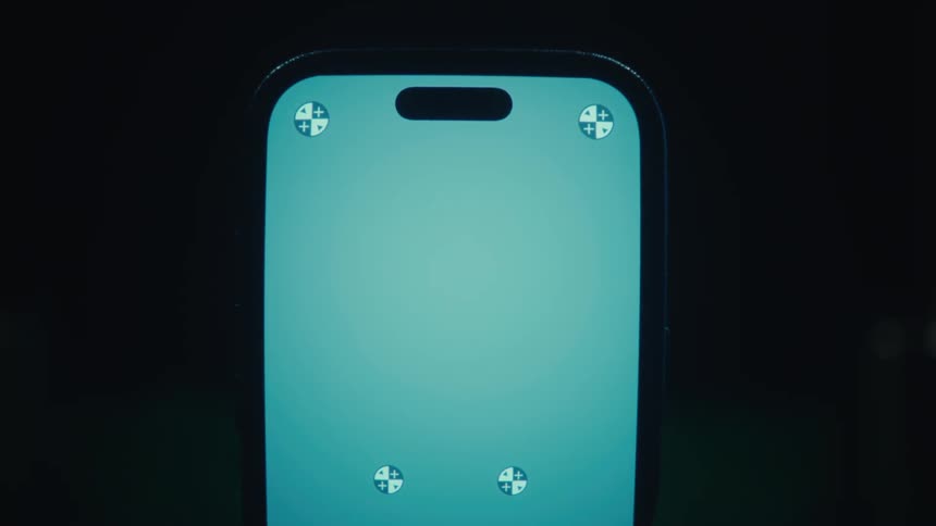 A closeup shot of a smartphone with a bright light blue screen featuring several small tracking markers positioned against a dark background