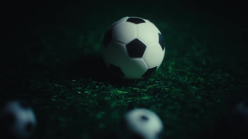 A group of tiny soccer ball sits on a patch of green grass under a dark atmospheric light