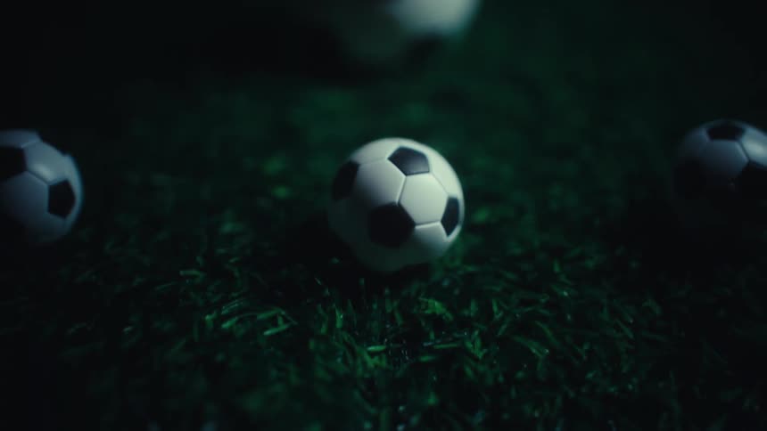 Large and small balls with a soccer pattern sit on artificial turf at night