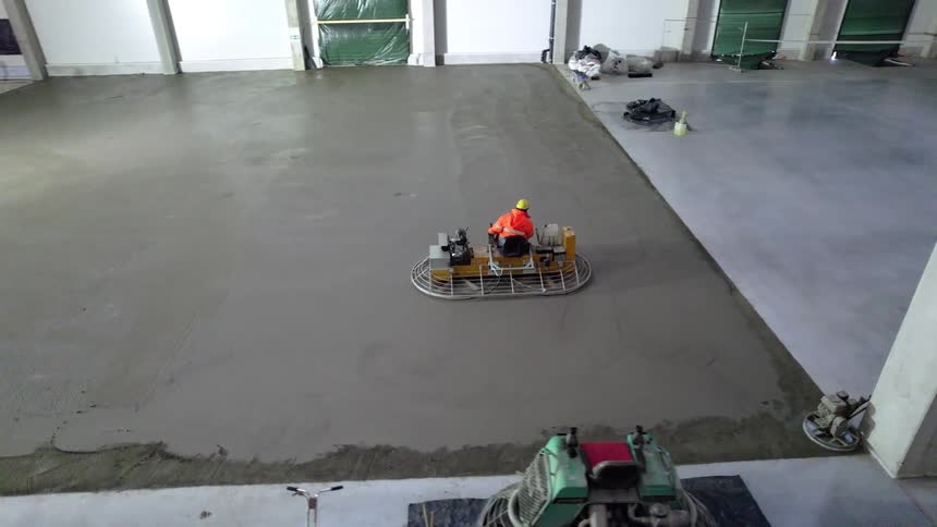 Worker in orange jacket operates trowel on wet concrete at industrial site