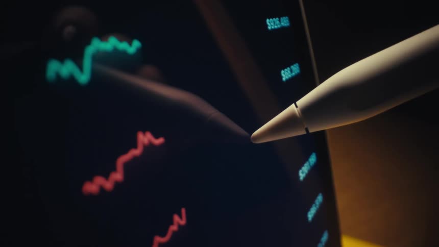 A stylus points at colorful fluctuating line graphs displayed on a digital screen suggesting data analysis or market tracking
