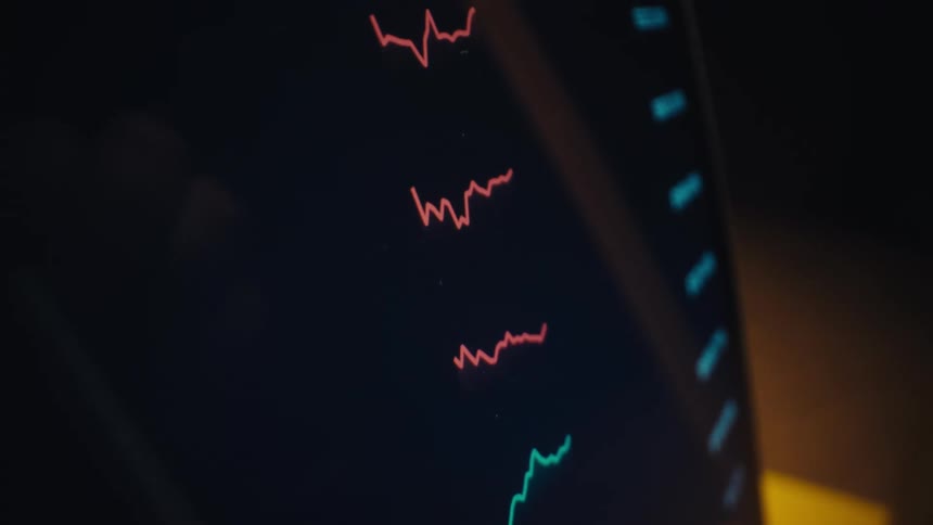 A stylus points at colorful fluctuating line graphs displayed on a digital screen suggesting data analysis or market tracking