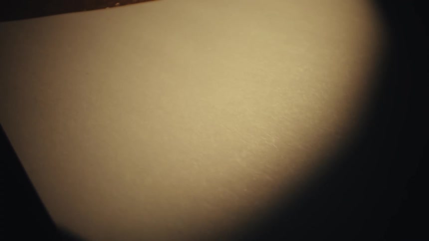 Closeup of a hand presses a stamp onto a plain white piece of paper in low light