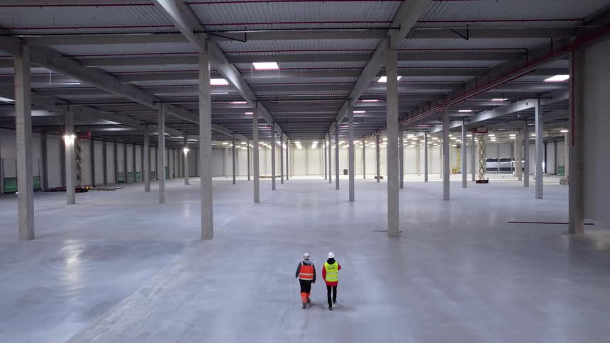 Workers wearing safety gear walking inside a large empty industrial warehouse