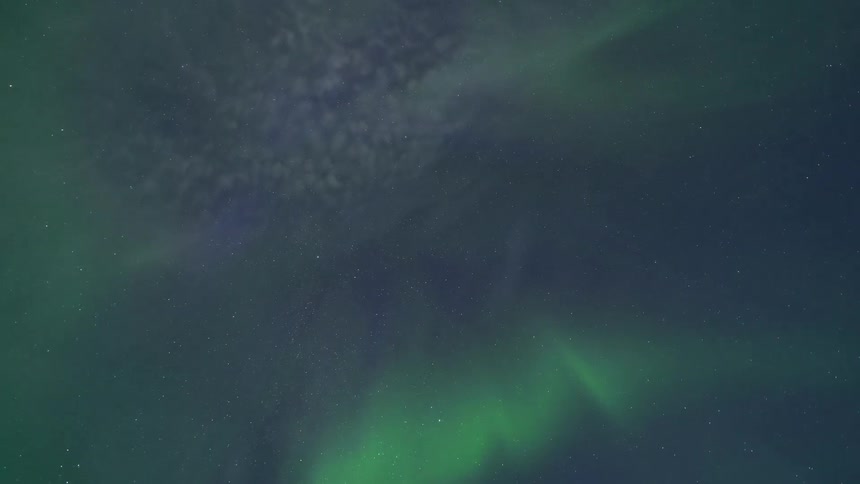 Soft green aurora lights drift across a dark starspeckled night sky