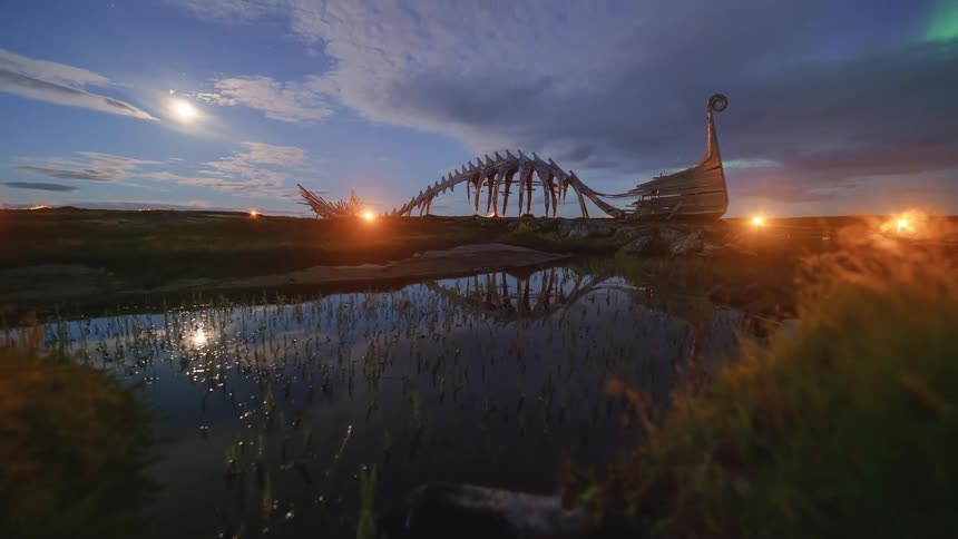 Viking shipshaped sculptural installation beside a reflective pool with artificial lighting at dusk