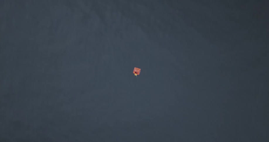 A small orange object floats alone in a vast expanse of dark blue water emphasizing its isolation