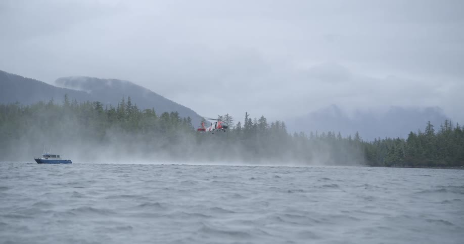 Boat sailing on rough water off the coast as a helicopter hovers in the air