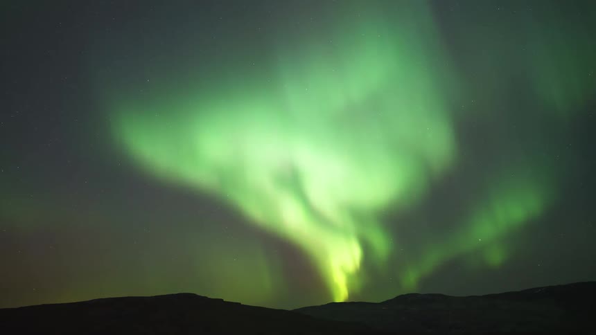 The glowing green lights of the aurora borealis move across the night sky