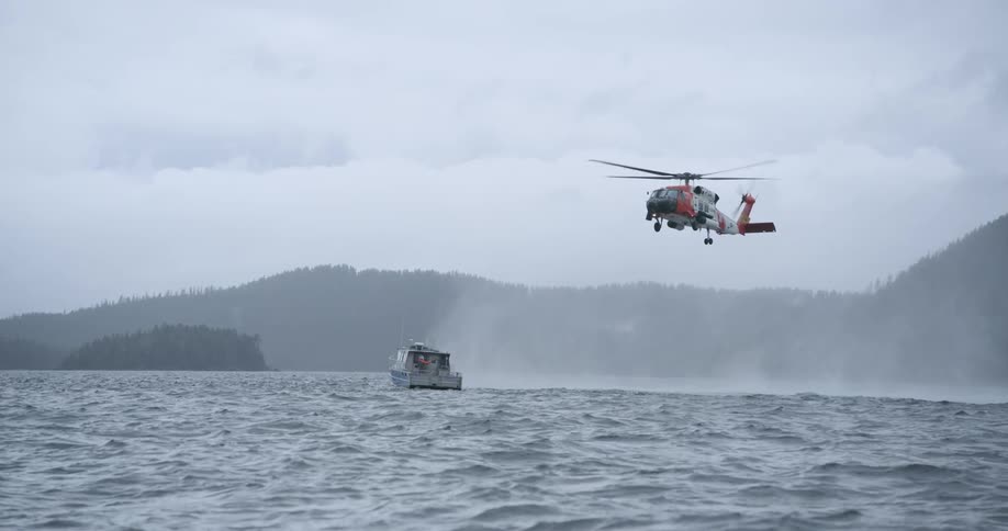 Boat sailing on rough water off the coast as a helicopter hovers in the air
