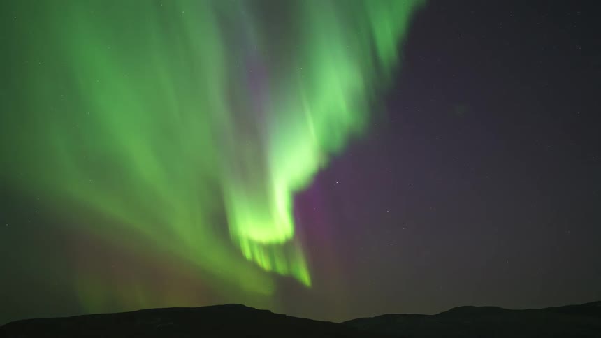Colorful glowing lights of the aurora borealis move over mountains in the night sky