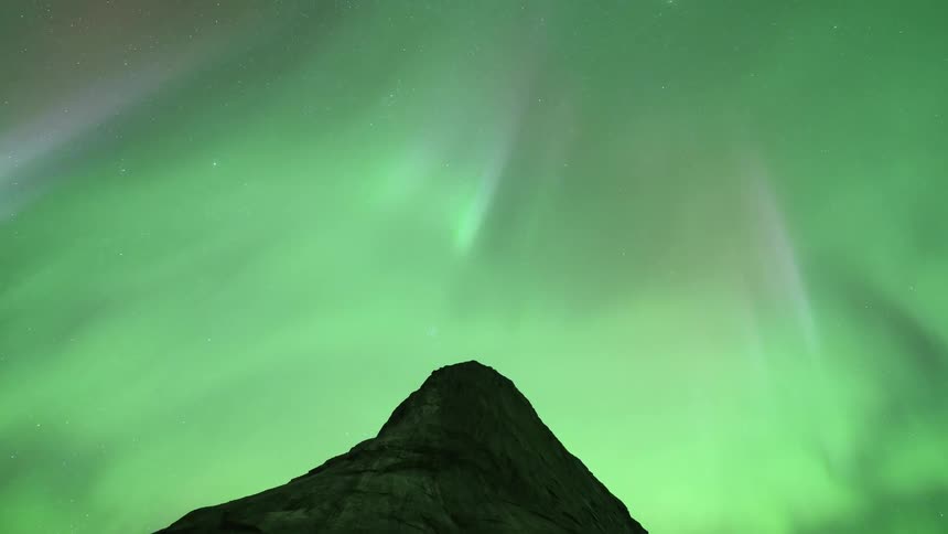 The green glow of the northern lights illuminates the night sky over a mountain