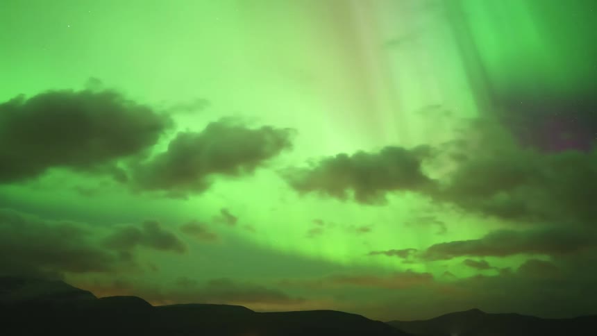 Northern lights illuminating the night sky with green purple and pink bands above a dark landscape