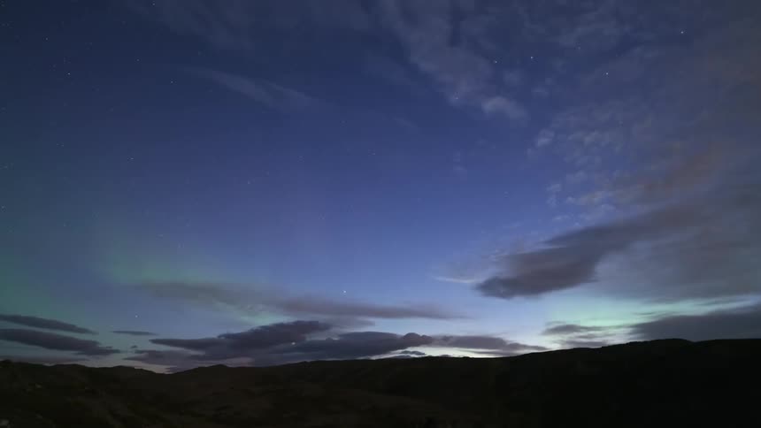 At sunset a hill rises gently from the wilderness its silhouette glowing in the fading orange light above it a soft green light hovers in the sky