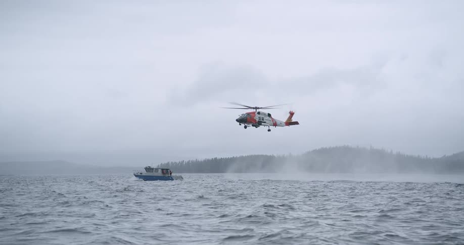 Boat sailing on rough water off the coast as a helicopter hovers in the air