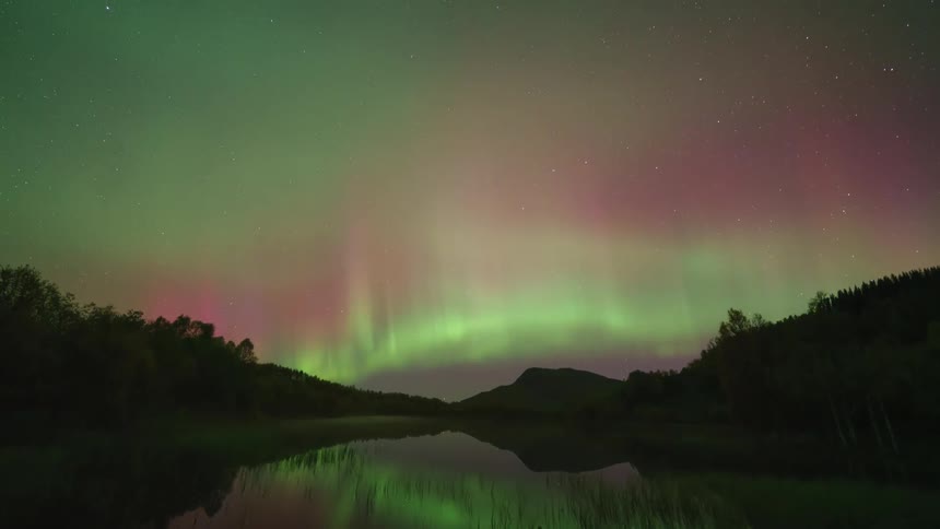 The flaring northern lights reflect on the stream