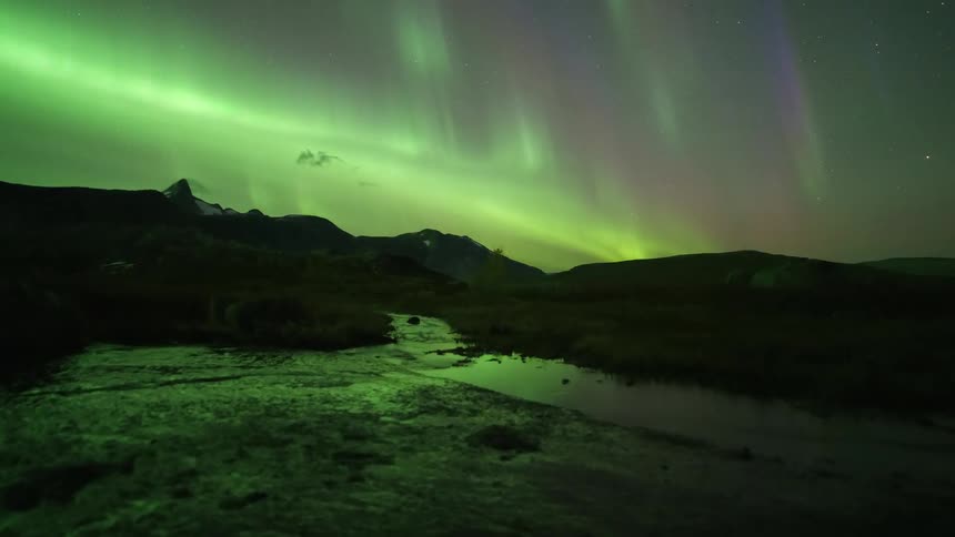 Mountains along the coast as the glowing lights of the aurora borealis move across the sky