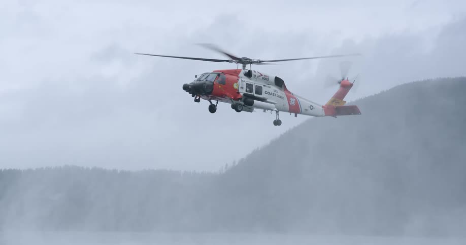 A us coast guard helicopter hovers low over the water its powerful rotors kicking up a dense mist against a backdrop of fogshrouded hills