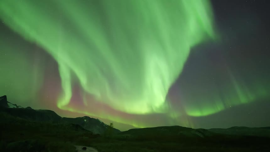 The colorful glowing lights of the aurora borealis illuminate the night sky over mountains along the coast