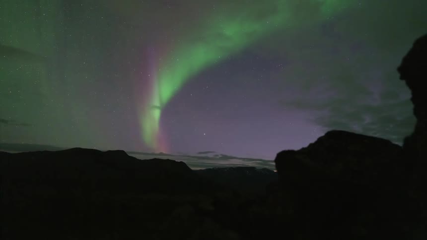 The green northern lights shine over the dark mountains