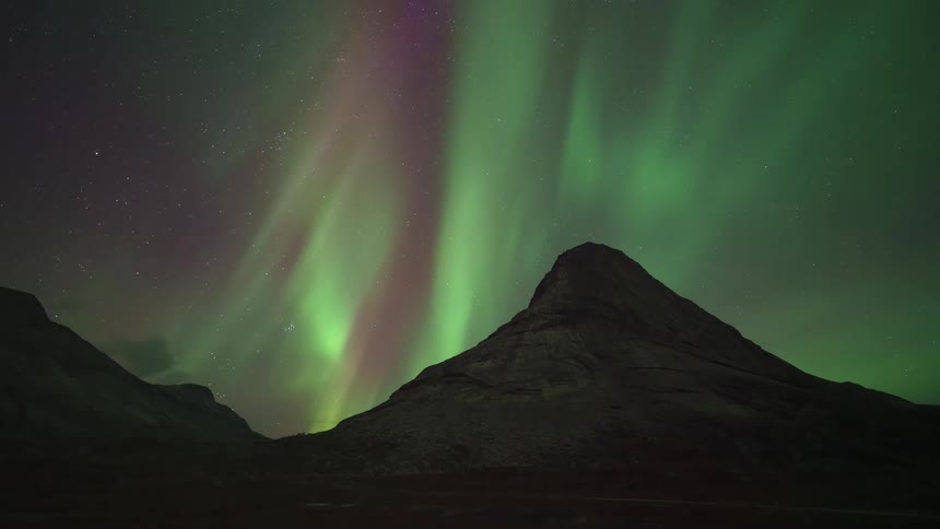 The northern lights shine and wave above the mountain peak