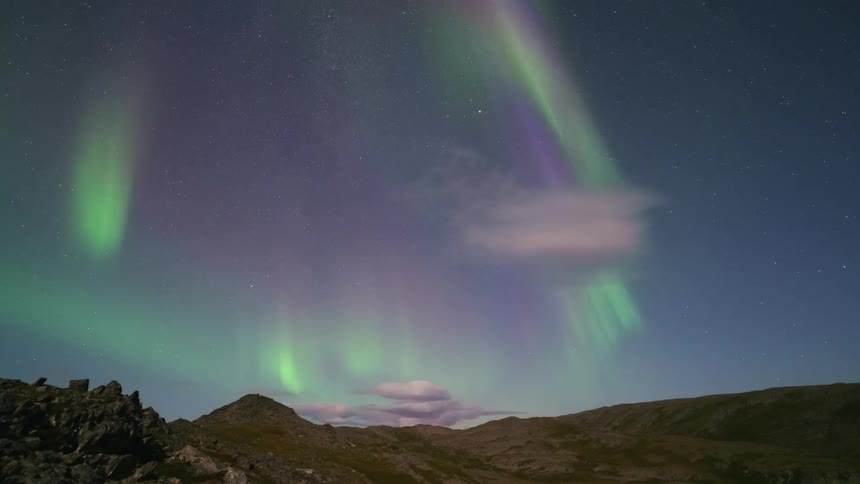 The northern lights glow as they move over the mountain landscape