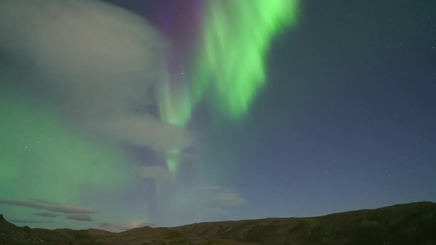 Aurora borealis with vertical green curtains over elevated terrain at night