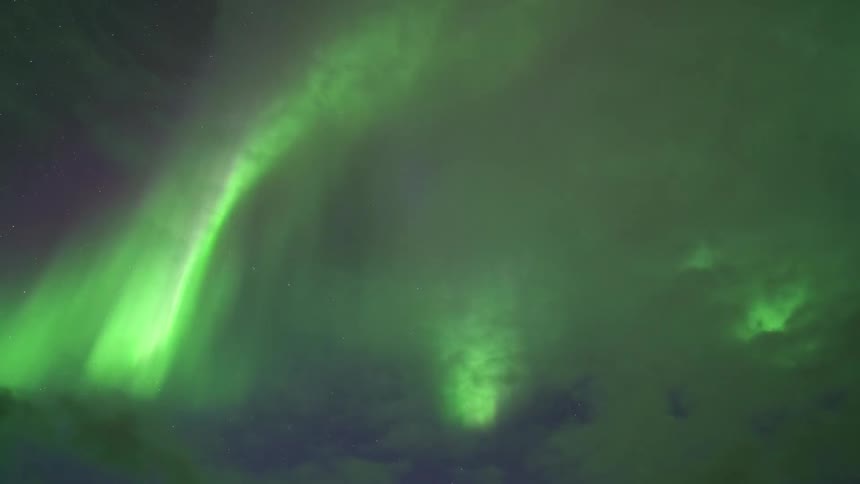 Aurora borealis with diffuse green bands among clouds at night