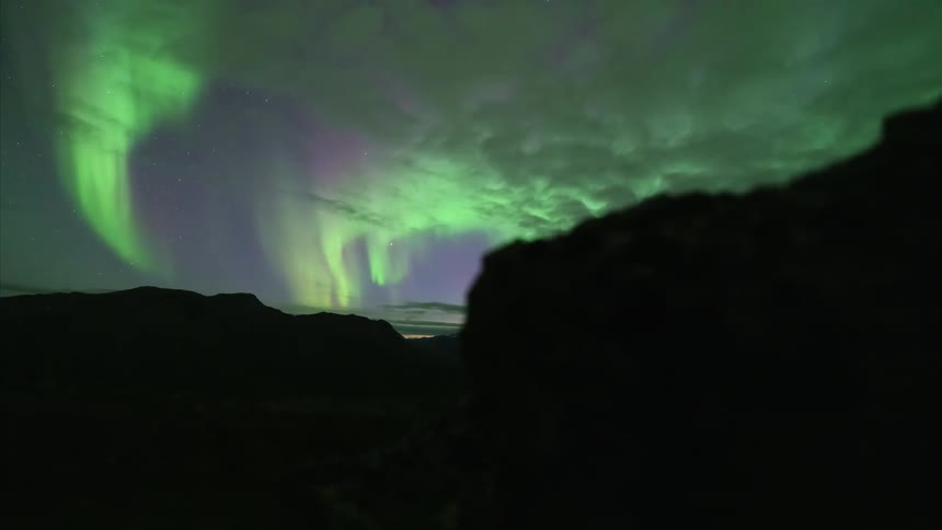 The northern lights shine green on the mountains