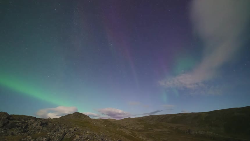 The northern lights are bright in the sky above the hills