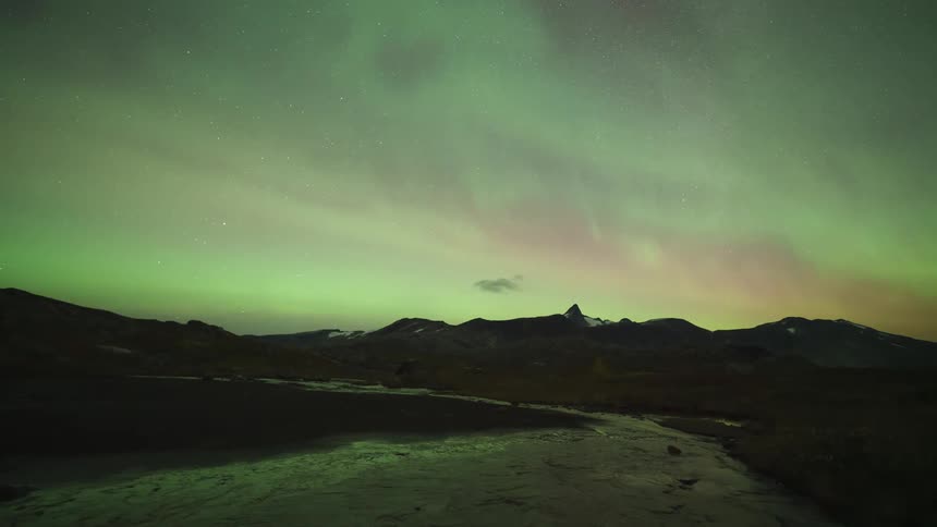 Soft aurora borealis on the horizon above a dark mountain range and open terrain at night