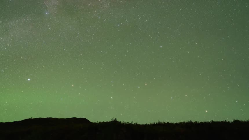 The green glow of the northern lights moves over a starry sky until daylight