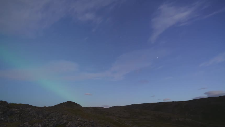 Northern lights glow as they move over the mountain landscape until daylight