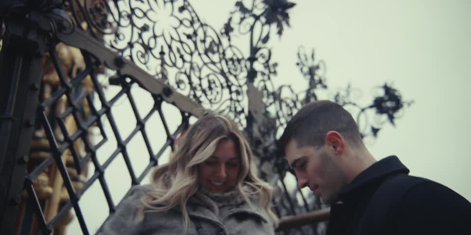 A happy young woman playfully touches the intricate ironwork of a gate in a historic city square laughing and talking with her partner as they explore