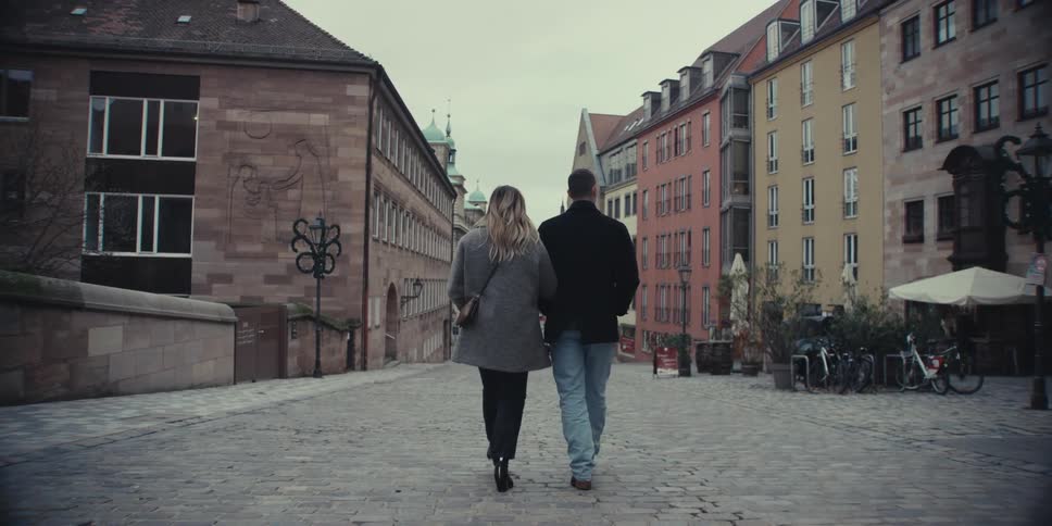 A couple walks down a cobblestone street lined with historic colorful buildings on an overcast day