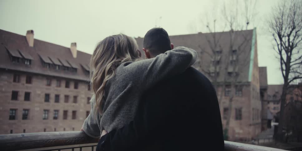 Couple embracing while leaning on a bridge with historic buildings in the background