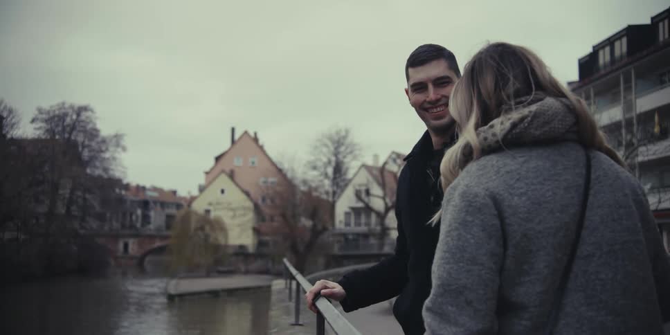 Man and woman standing next to a railing overlooking a canal through the neighborhood as he kisses her