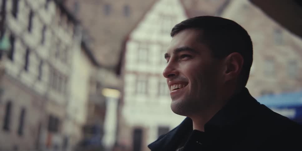 Traditional halftimbered buildings line a historic street with a blurred figure in the foreground and blurred figures in the background adding a sense of everyday life to the scene