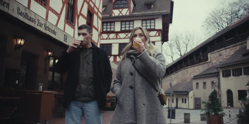 A smiling couple enjoying drinks while walking through a historic european street